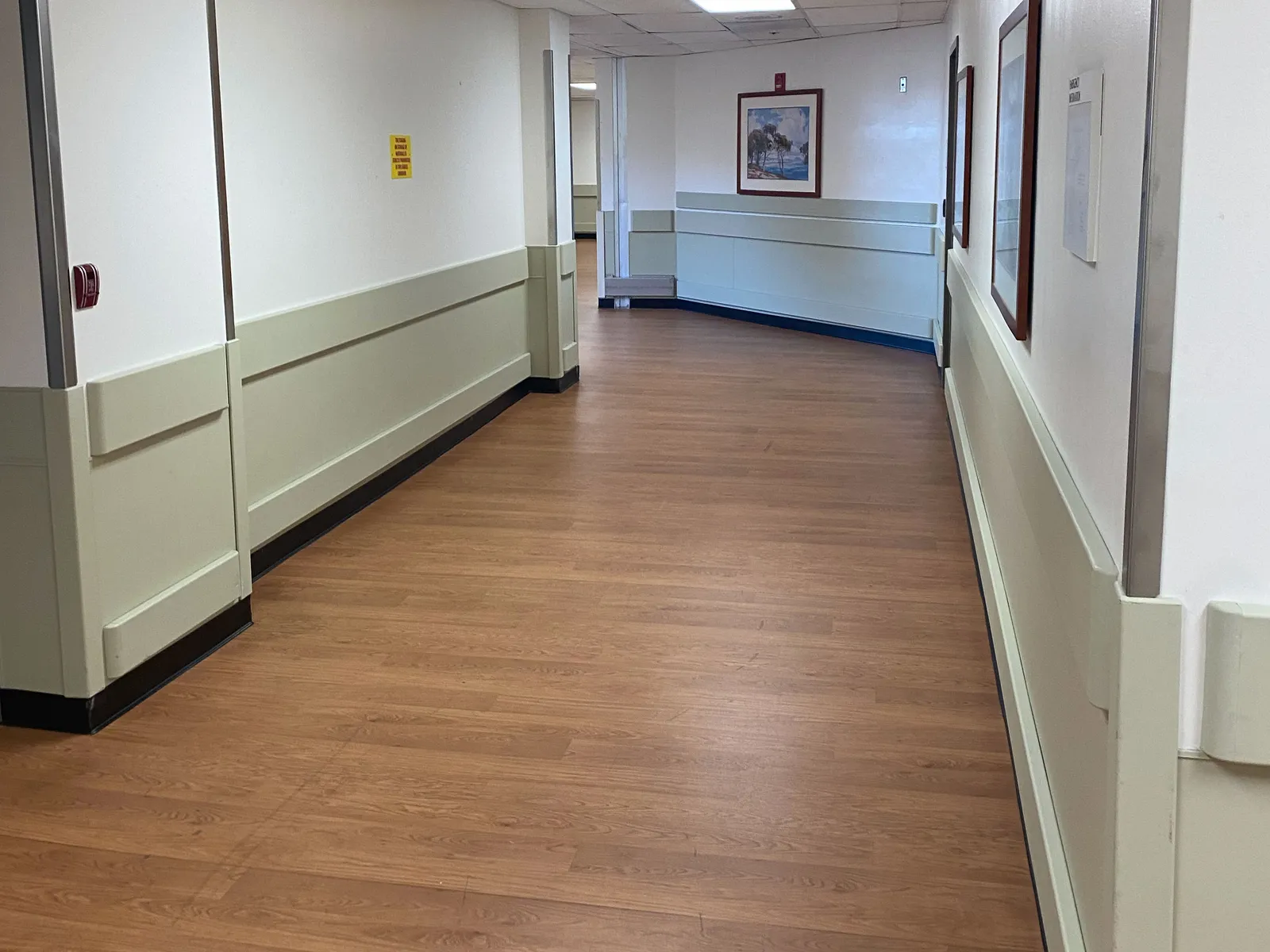 Renovated hospital inpatient corridor with wood-look flooring, wall protection, and framed artwork